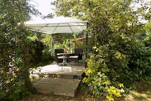 An outdoor patio with a table and chairs under a canopy, surrounded by dense foliage. - Holiday apartment with 1 bedroom (Freinsheim)