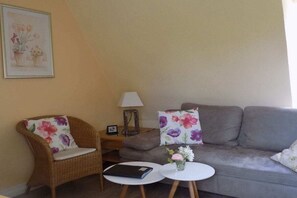 A living room with a grey sofa, a wicker chair, a small table, and a lamp. - Holiday apartment with 1 bedroom (Freinsheim)