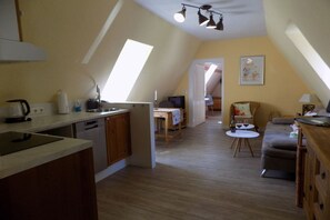 A compact kitchen with a dining area, a small table with wine glasses, and a sofa. - Holiday apartment with 1 bedroom (Freinsheim)