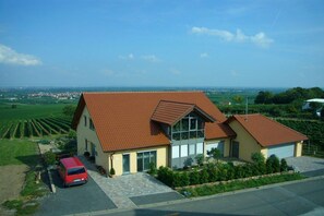 A two-story house with a red-tiled roof, a driveway, and a red car parked in front. - Holiday apartment with 0 bedrooms (Herxheim)