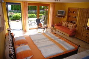 A bedroom with a bed, a sofa, a television, and a view of a garden through a sliding door. - Holiday apartment with 0 bedrooms (Herxheim)