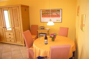 Ein Essbereich mit einem runden Tisch, Stühlen, einer Weinflasche und einem Blumenstrauß.