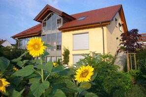 Ein zweistöckiges Haus mit einem roten Ziegeldach, großen Fenstern und einem Garten mit Sonnenblumen.
