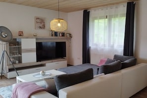 A modern living room with a flat-screen TV, a sofa, a coffee table, and a pendant light. - Holiday apartment with 3 bedrooms (Oberzent Airlenbach)