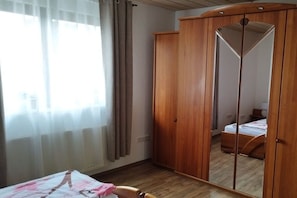 A room with a bed, a wooden wardrobe, and a mirror reflecting the room. - Holiday apartment with 3 bedrooms (Oberzent Airlenbach)