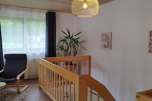 Een kamer met een houten kinderbedje, een potplant, een stoel en een hanglamp.