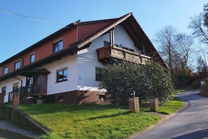 Een twee verdiepingen tellend huis met een schuin dak, een balkon en een verzorgd gazon.