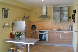 A compact kitchen with a stove, oven, and a coffee maker. There is a small dining area with stools and a vase of flowers. - "Chargund": Holiday apartment "Chardonnay" (Herxheim)