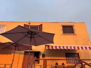 Um edifício com um grande guarda-sol, escadaria de madeira e uma janela com grades.
