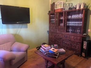 A living room with a flat-screen TV, a wooden cabinet with glassware, a sofa, and a coffee table with books. - VILLA_mom (CN)