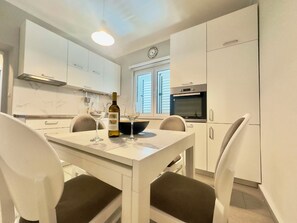 Une cuisine moderne avec des meubles blancs, une table à manger avec quatre chaises et une bouteille de vin posée sur la table.