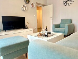 Un salon moderne avec un téléviseur à écran plat, une table basse sur laquelle se trouvent une bouteille et des verres, et deux canapés bleu clair.