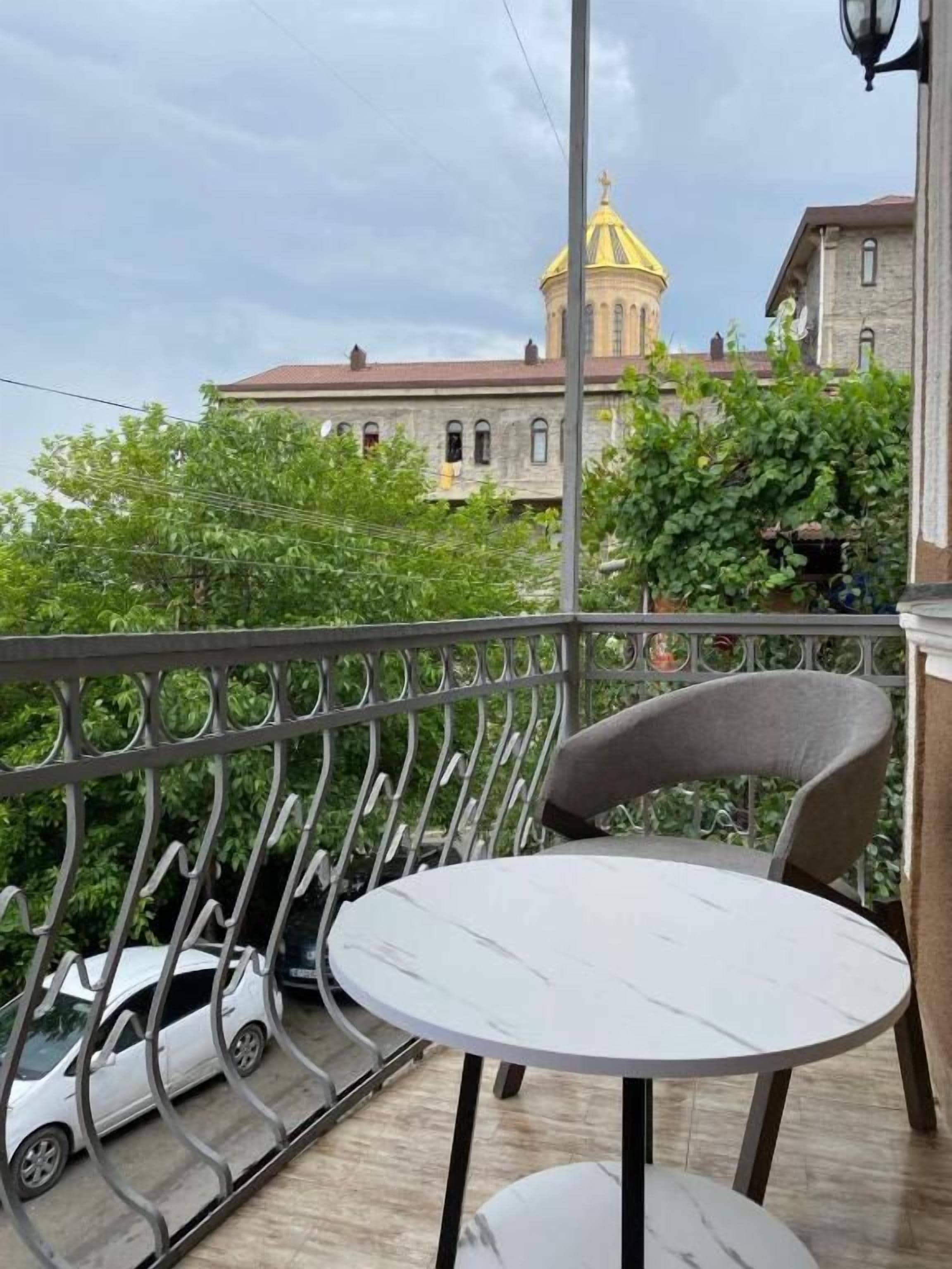Un balcon avec une table ronde et des chaises, donnant sur un bâtiment doté d’un dôme jaune et d’un toit rouge.