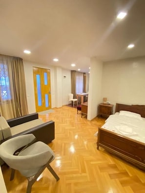 Quarto de hotel com cama, sofá, poltrona, escrivaninha e mesa de cabeceira.