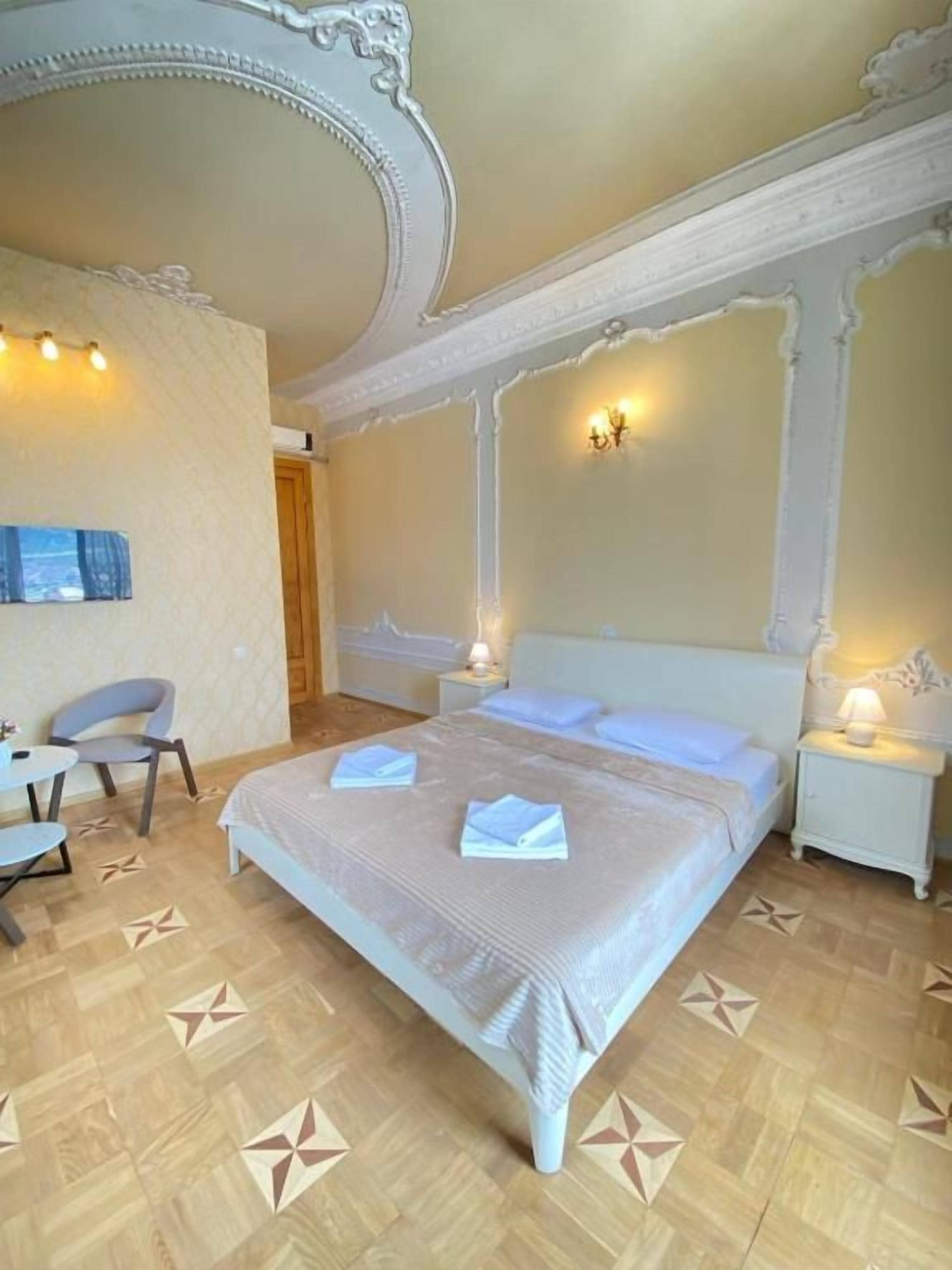Quarto de hotel com cama, mesas de cabeceira, uma cadeira e uma pequena mesa.