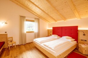 A bedroom with a wooden ceiling, a bed with a red headboard, a window with curtains, and a small wooden chair. - Apartment in Lajen with swimming pool (Lajen)