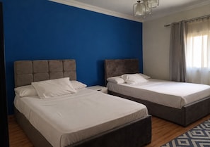 A room with two beds, a blue wall, and a window with curtains. - Luxury Apartment in New Cairo (Cairo Governorate)