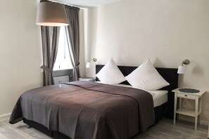 A hotel room with a large bed, two bedside tables, a window with curtains, and a lamp. - Holiday apartment with 3 bedrooms (Freinsheim)
