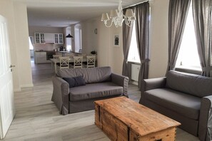 Een woonkamer met twee banken, een houten bijzettafeltje en een eethoek op de achtergrond.