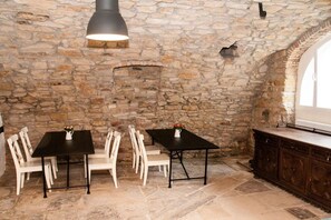 A stone-walled room with two tables and chairs, a hanging light fixture, and a wooden cabinet. - Holiday apartment with 3 bedrooms (Freinsheim)