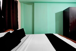 Uma cama com roupa de cama preta e branca, uma cabeceira de madeira e uma parede verde.