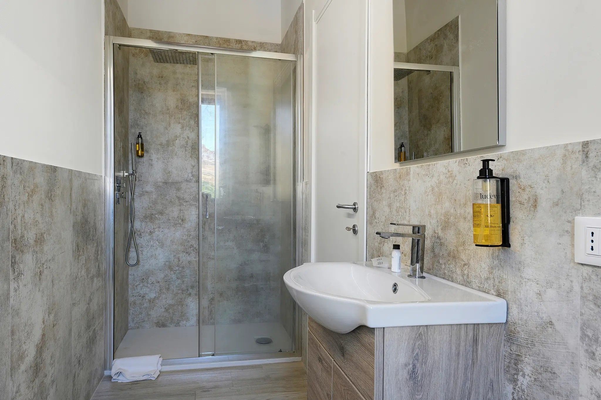 Une salle de bain moderne avec une douche à parois de verre, un lavabo blanc et un miroir au-dessus.
