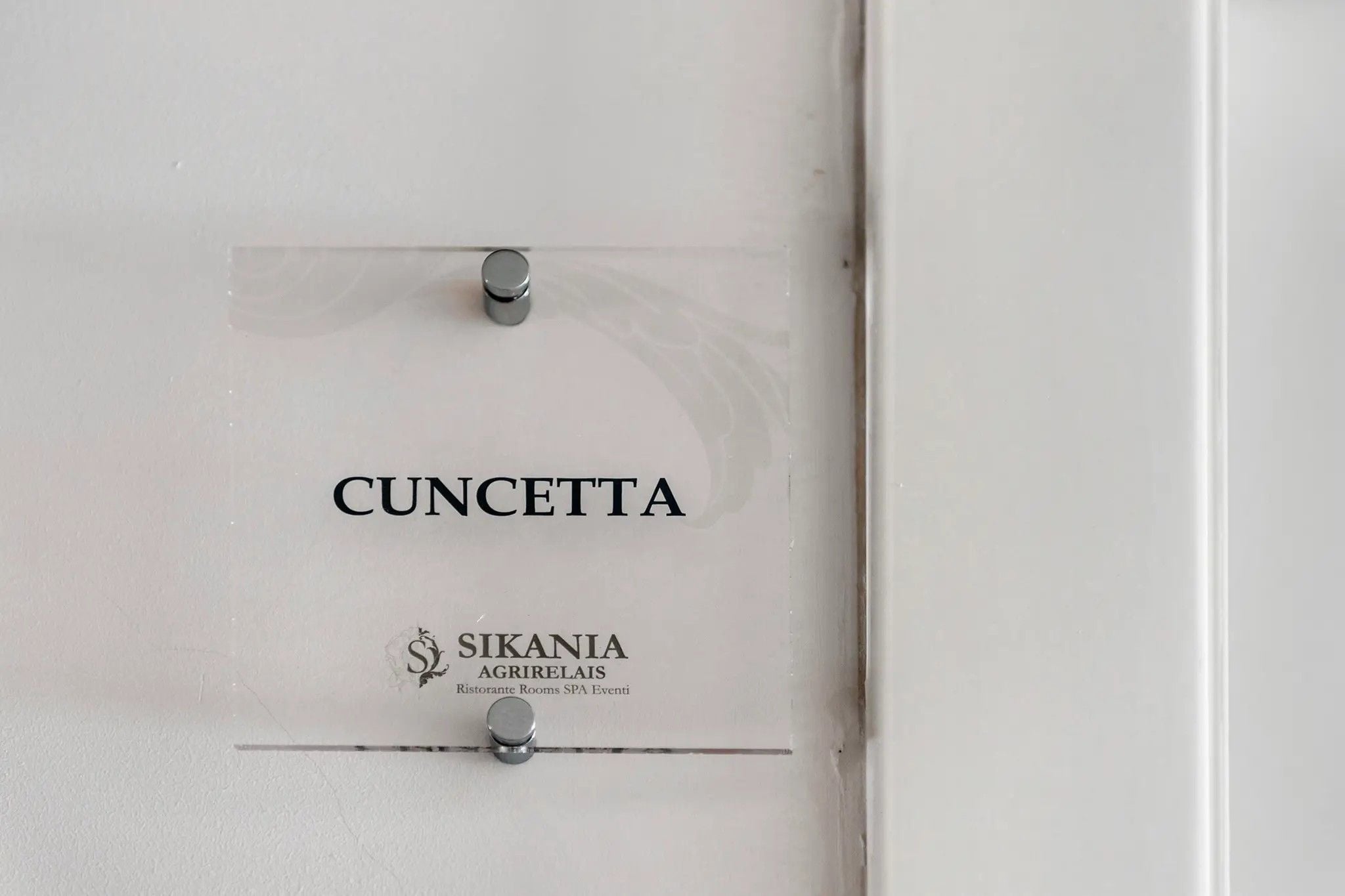 A white door with the name 'CUNCETTA' and the logo 'SIKANIA AGRIFRELAIS' indicating a restaurant and spa event.