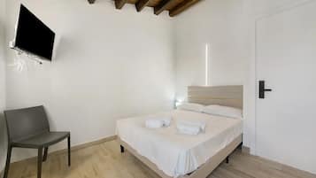 A bedroom with a bed, a chair, a flat-screen TV mounted on the wall, and a door.