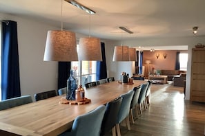 Ein geräumiger Essbereich mit einem langen Holztisch, blauen Polsterstühlen und hängenden Lampen.
