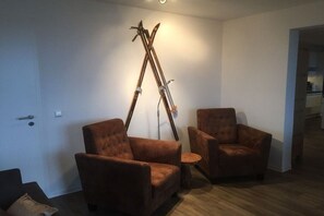 Ein Zimmer mit zwei braunen Sesseln, einem kleinen runden Tisch und einem Paar Ski, die an der Wand lehnen.