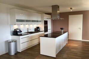 Eine moderne Küche mit weißen Schränken, einer zentralen Kochinsel, Edelstahlgeräten und einem Mülleimer.