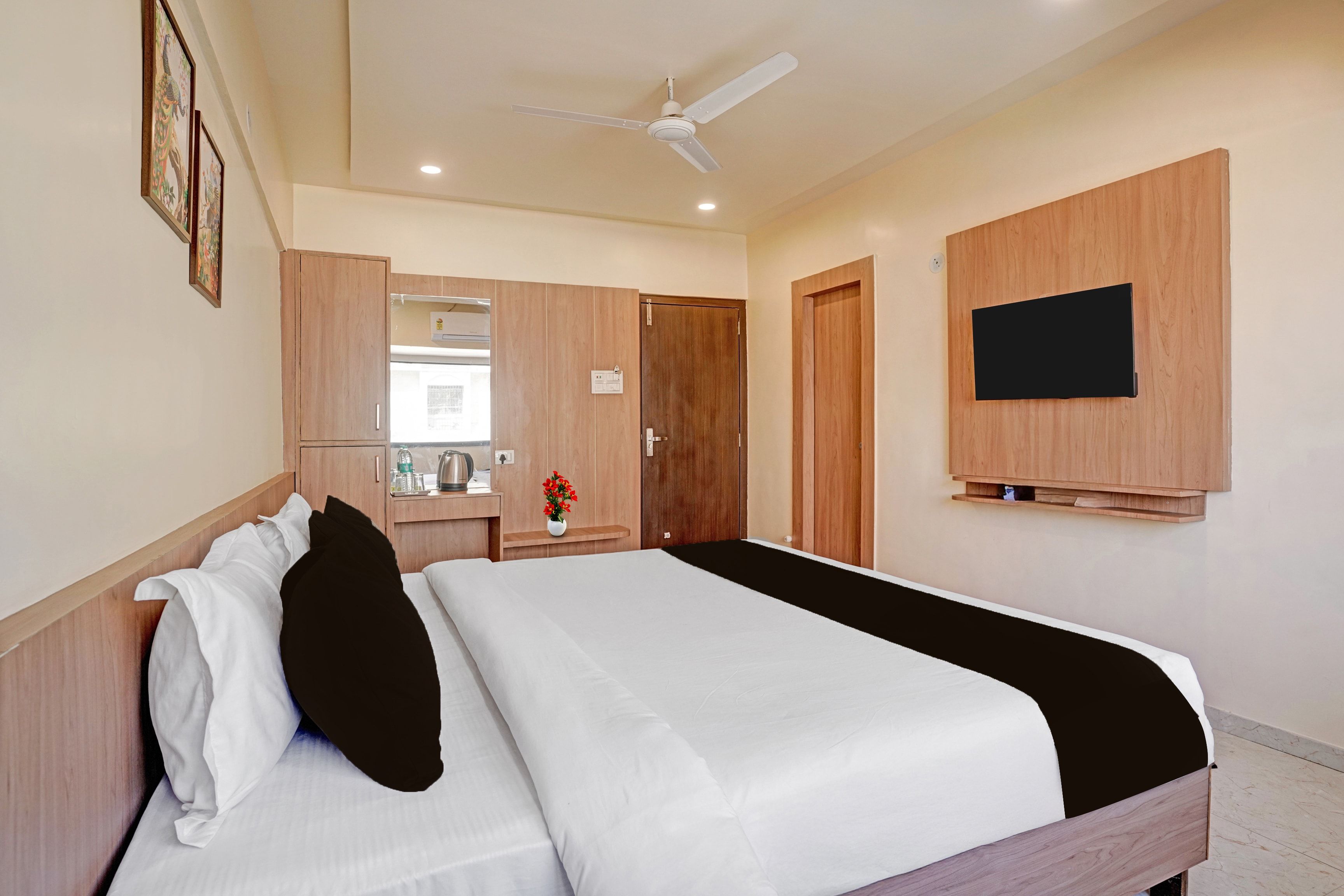 A hotel room with a bed, a wardrobe, a mirror, a television, and a ceiling fan.