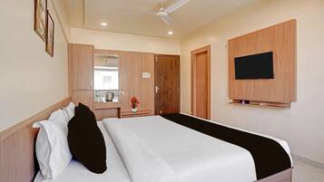 A hotel room with a bed, a wardrobe, a mirror, a television, and a ceiling fan.