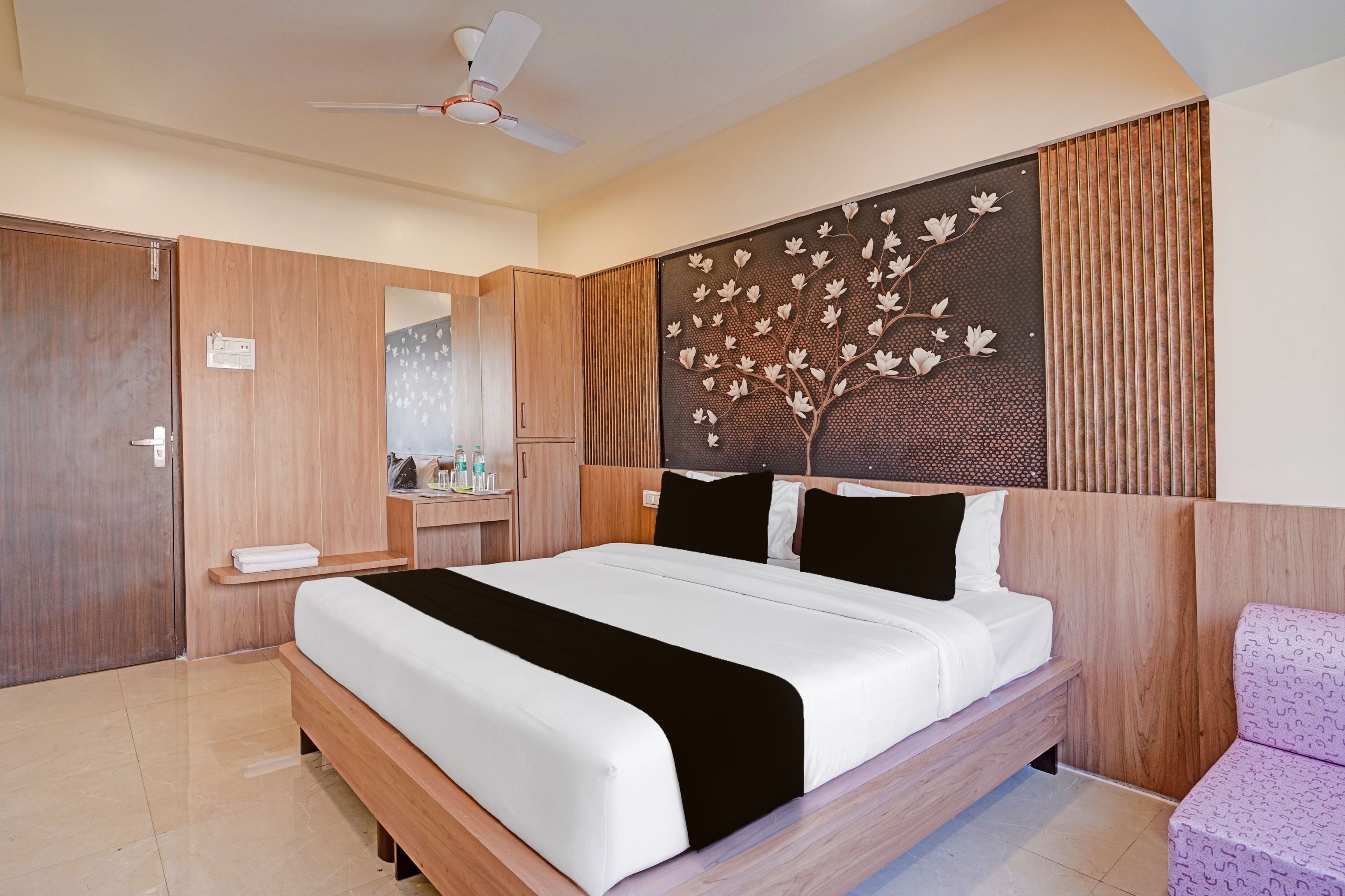 Habitación de hotel con una cama grande, cabecero de madera, ventilador de techo y un panel decorativo en la pared.