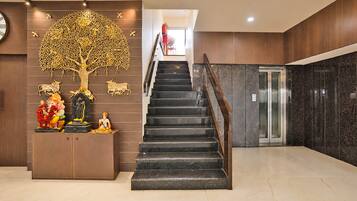 Una escalera conduce a un piso superior, flanqueada por una pared decorativa con un motivo de árbol y una estatua.