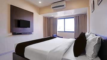 Una habitación de hotel con cama, televisión de pantalla plana montada en la pared, aire acondicionado y ventana con cortinas.