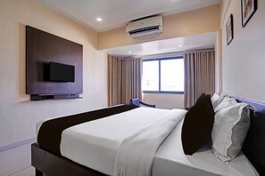 Una habitación de hotel con cama, televisión de pantalla plana montada en la pared, aire acondicionado y ventana con cortinas.