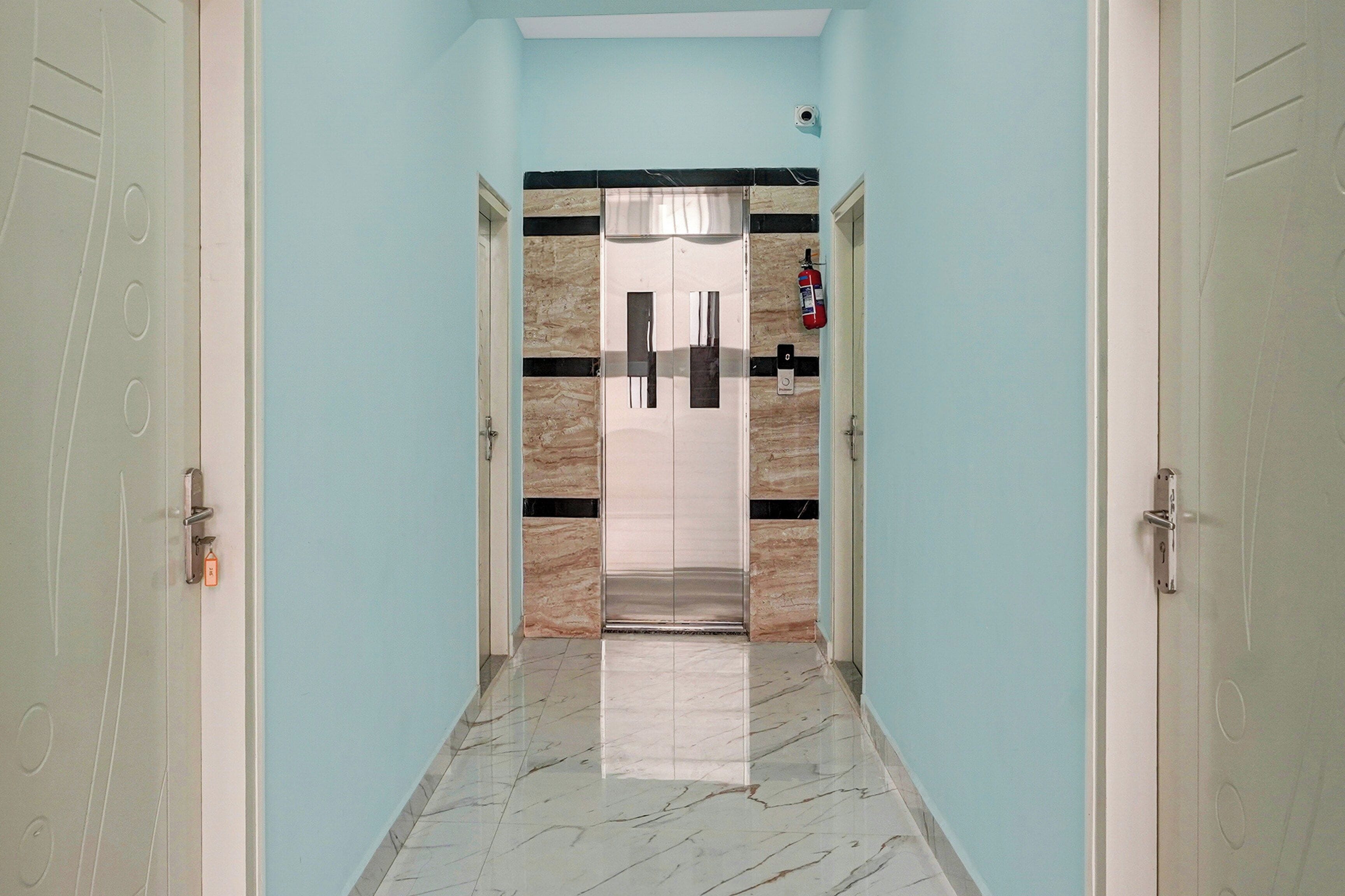 Un pasillo con piso de mármol, paredes azul claro y una puerta con un extintor montado.