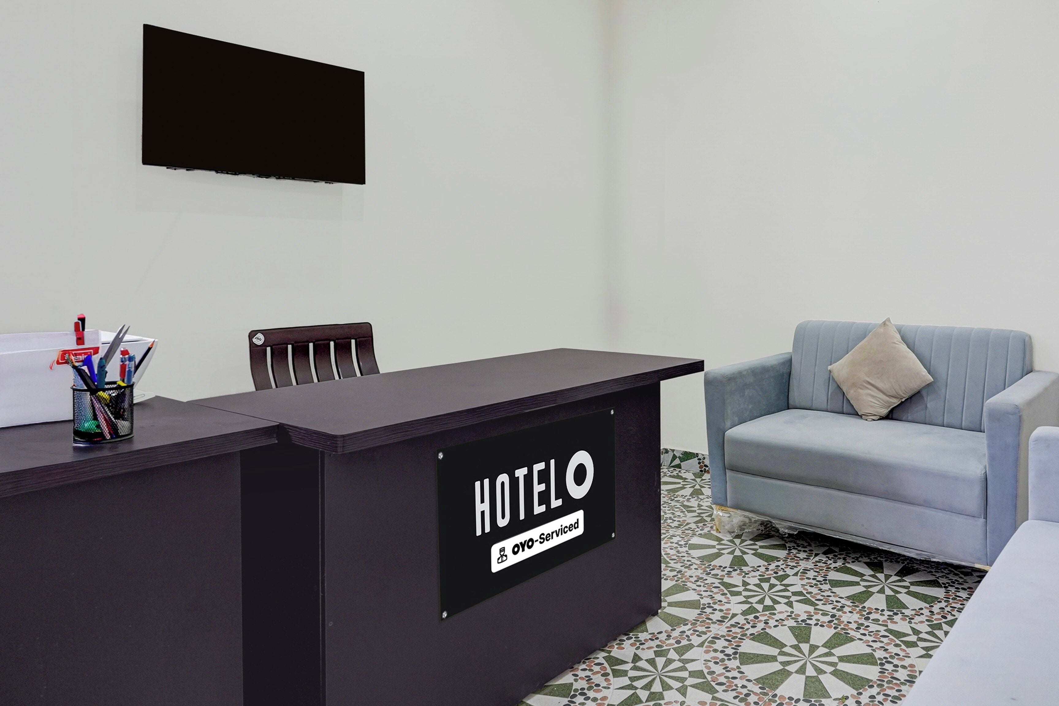 Mostrador de recepción de hotel con un letrero que dice 'HOTELO' y 'OYO-Service'. Hay una silla frente al mostrador y un sofá a la derecha.