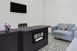 Mostrador de recepción de hotel con un letrero que dice 'HOTELO' y 'OYO-Service'. Hay una silla frente al mostrador y un sofá a la derecha.