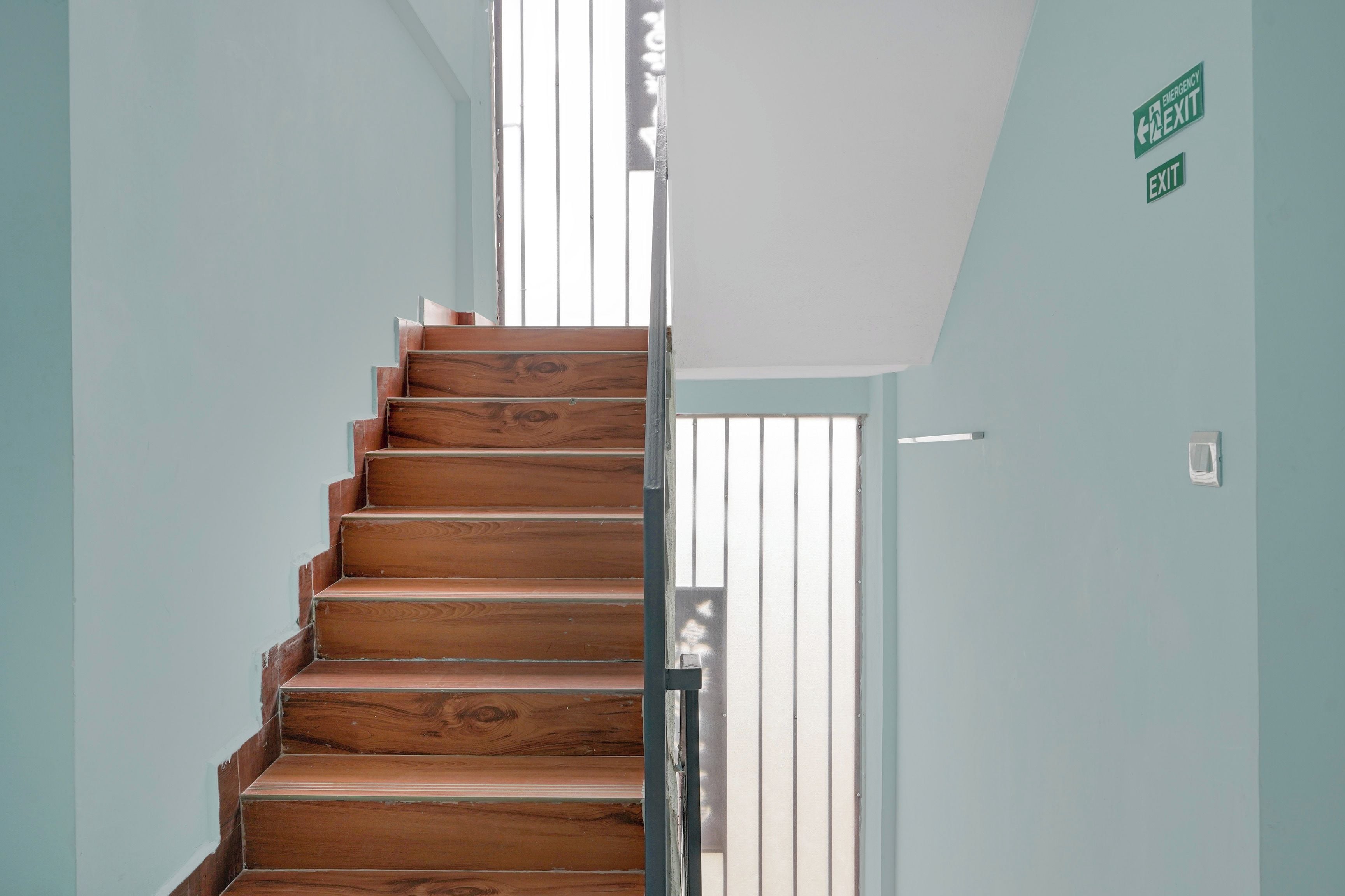 Una escalera de madera con barandilla de metal que conduce a una puerta con letrero de salida de emergencia.