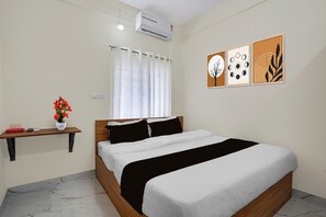 A bedroom with a bed, a nightstand, a window with curtains, an air conditioner, and wall art. - Hotel O Bidarahalli Main Road (Bangalore)