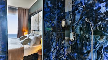 Una camera d'albergo con un letto, vista mare e bagno con parete in marmo.