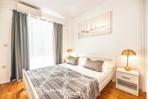 Een slaapkamer met een bed, twee nachtkastjes met lampen, een schilderij aan de muur en een raam met gordijnen.