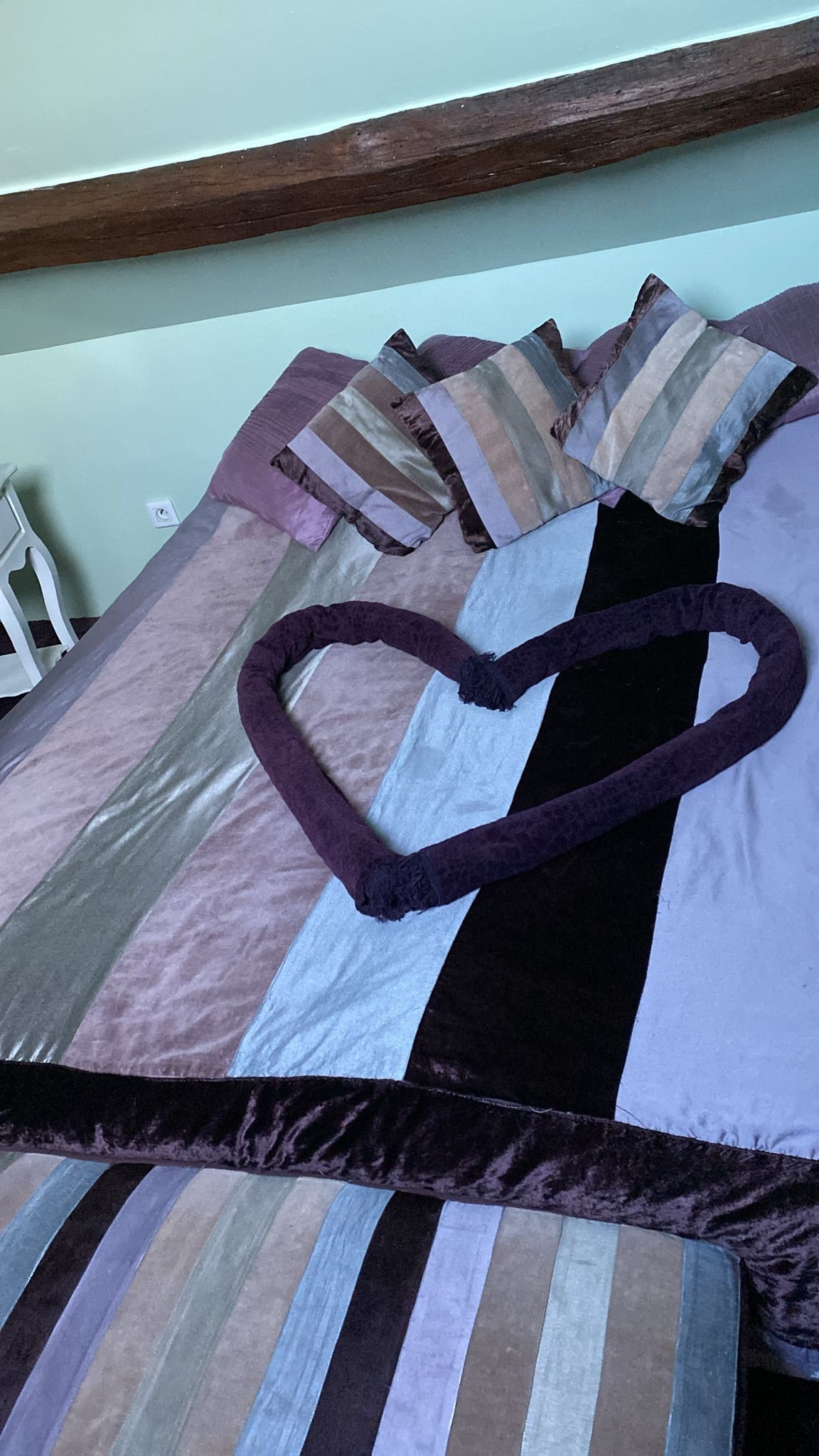 Uma cama com roupa de cama listrada, um travesseiro em formato de coração e uma cabeceira de madeira.