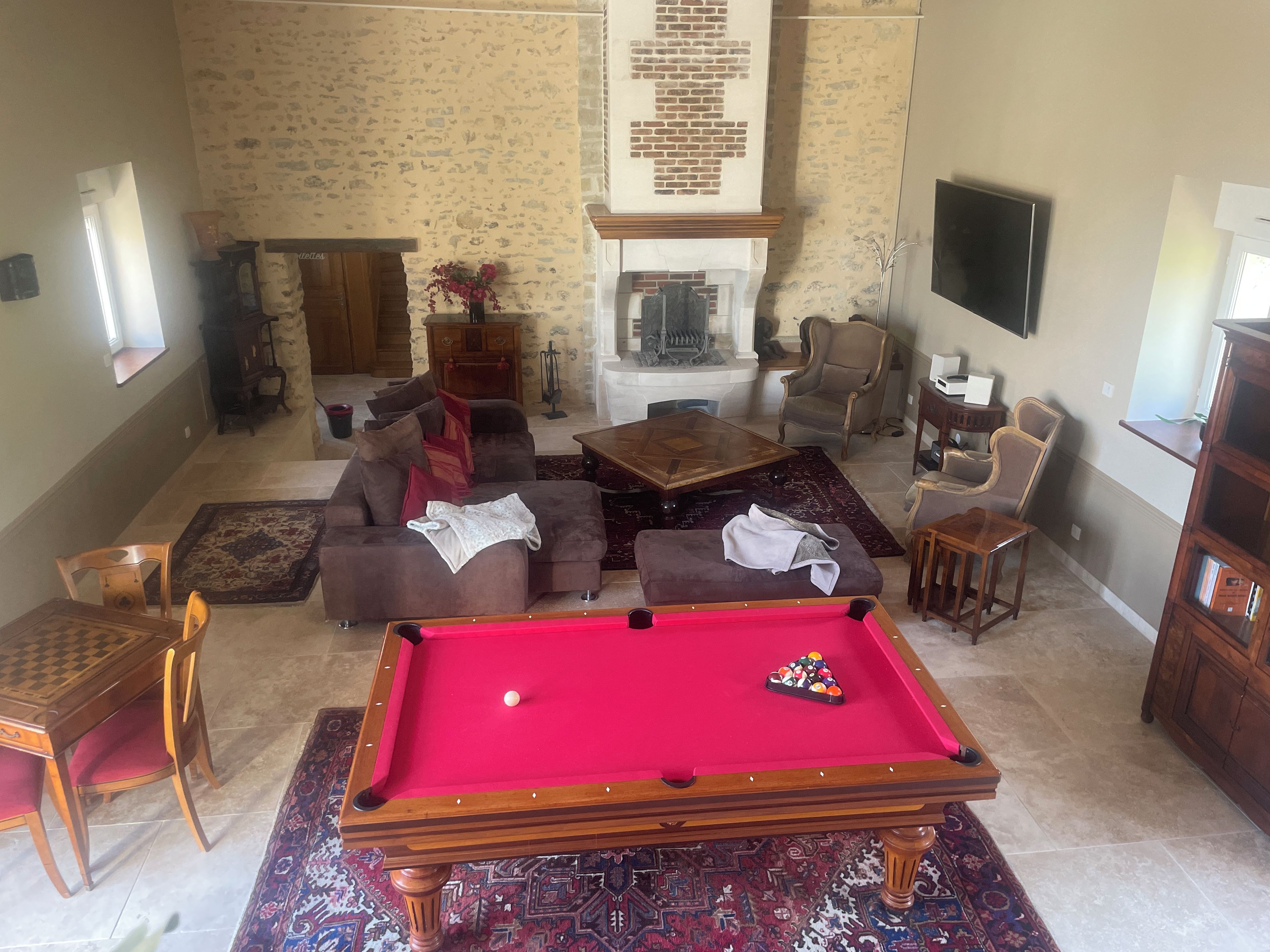 Een woonkamer met een pooltafel, banken, een open haard en een televisie.