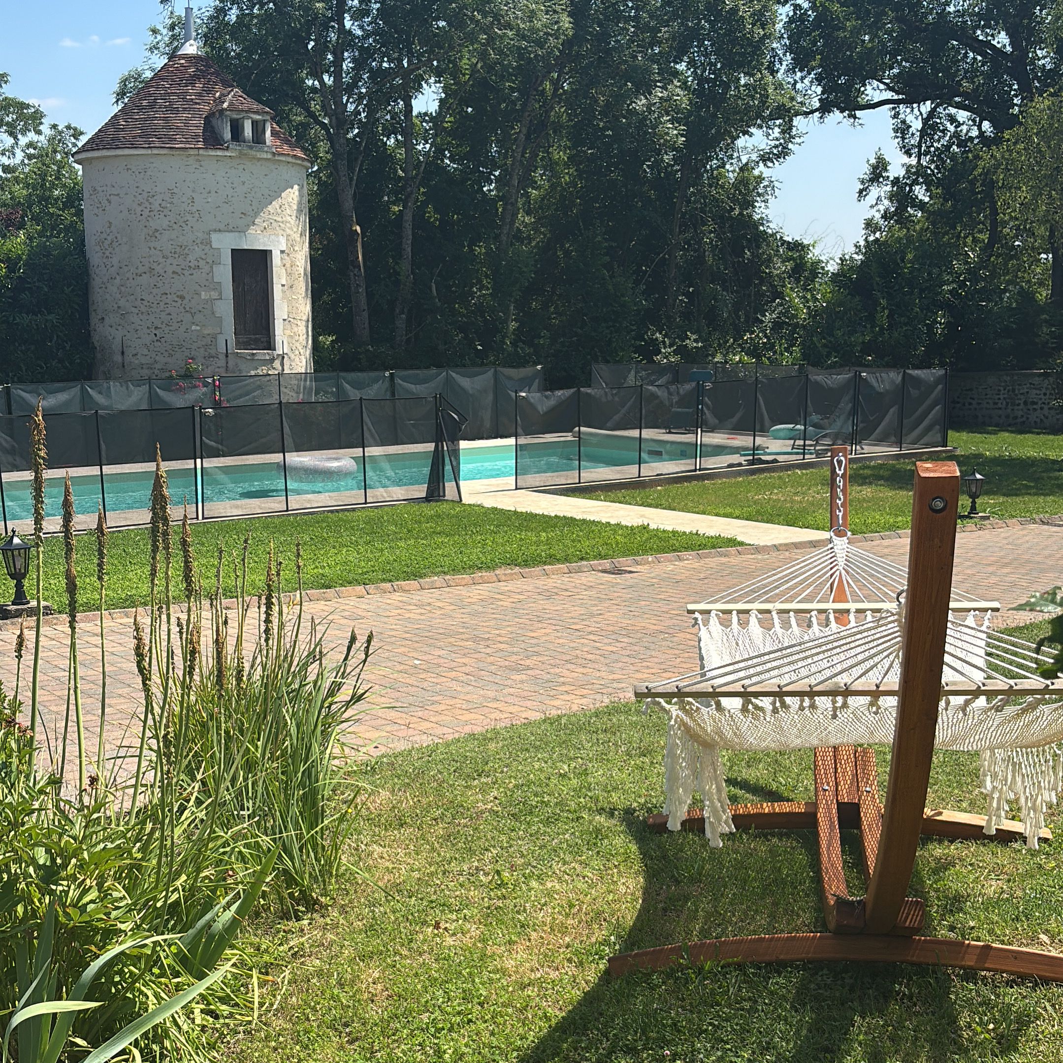 A pool area with a fenced pool, a hammock, and a small building.
