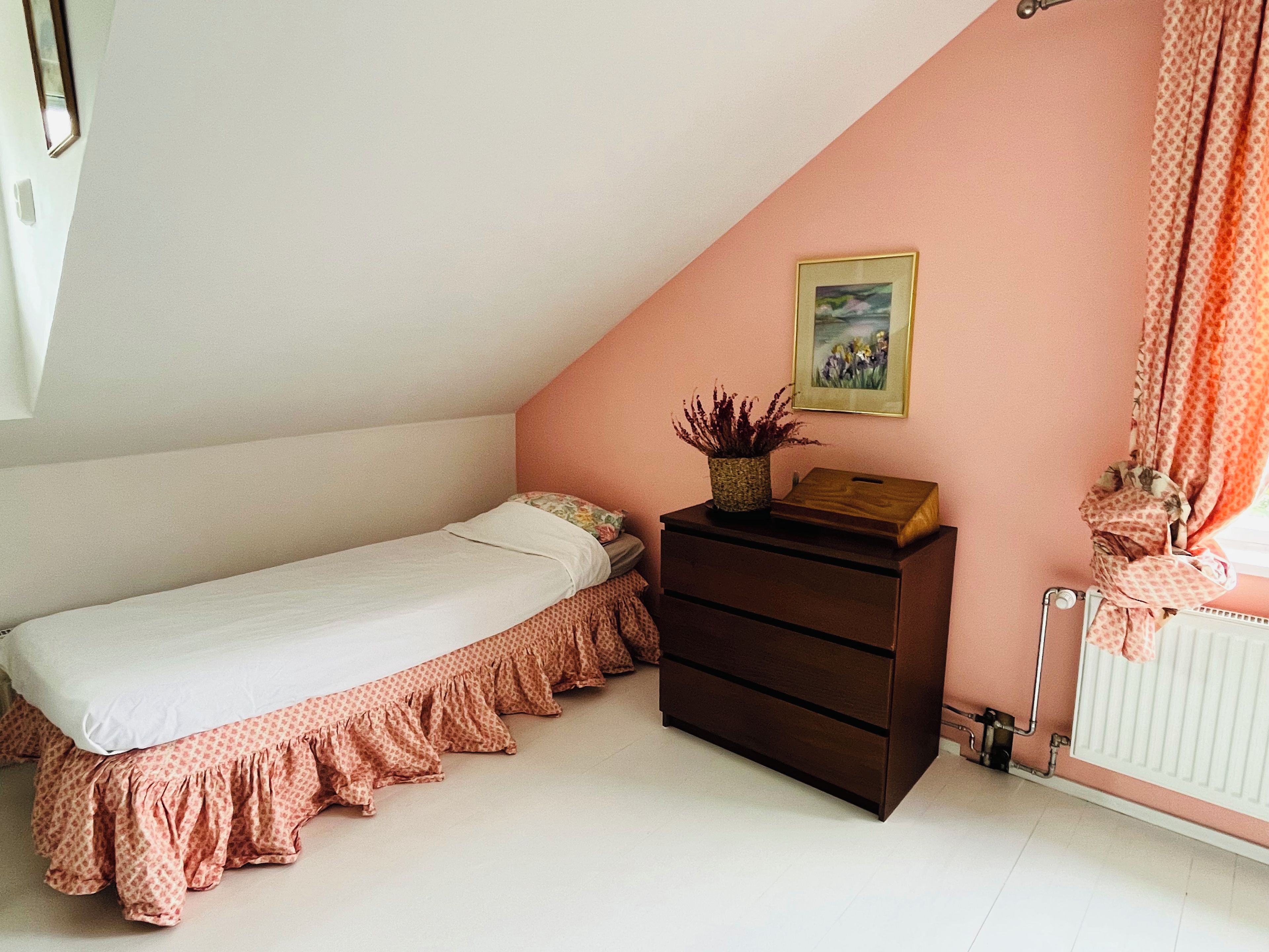 A bedroom with a single bed, a dresser, a radiator, and a framed picture on the wall.
