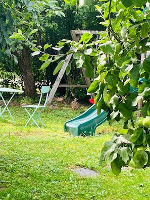 Um parquinho com escorrega, balanço e uma árvore.