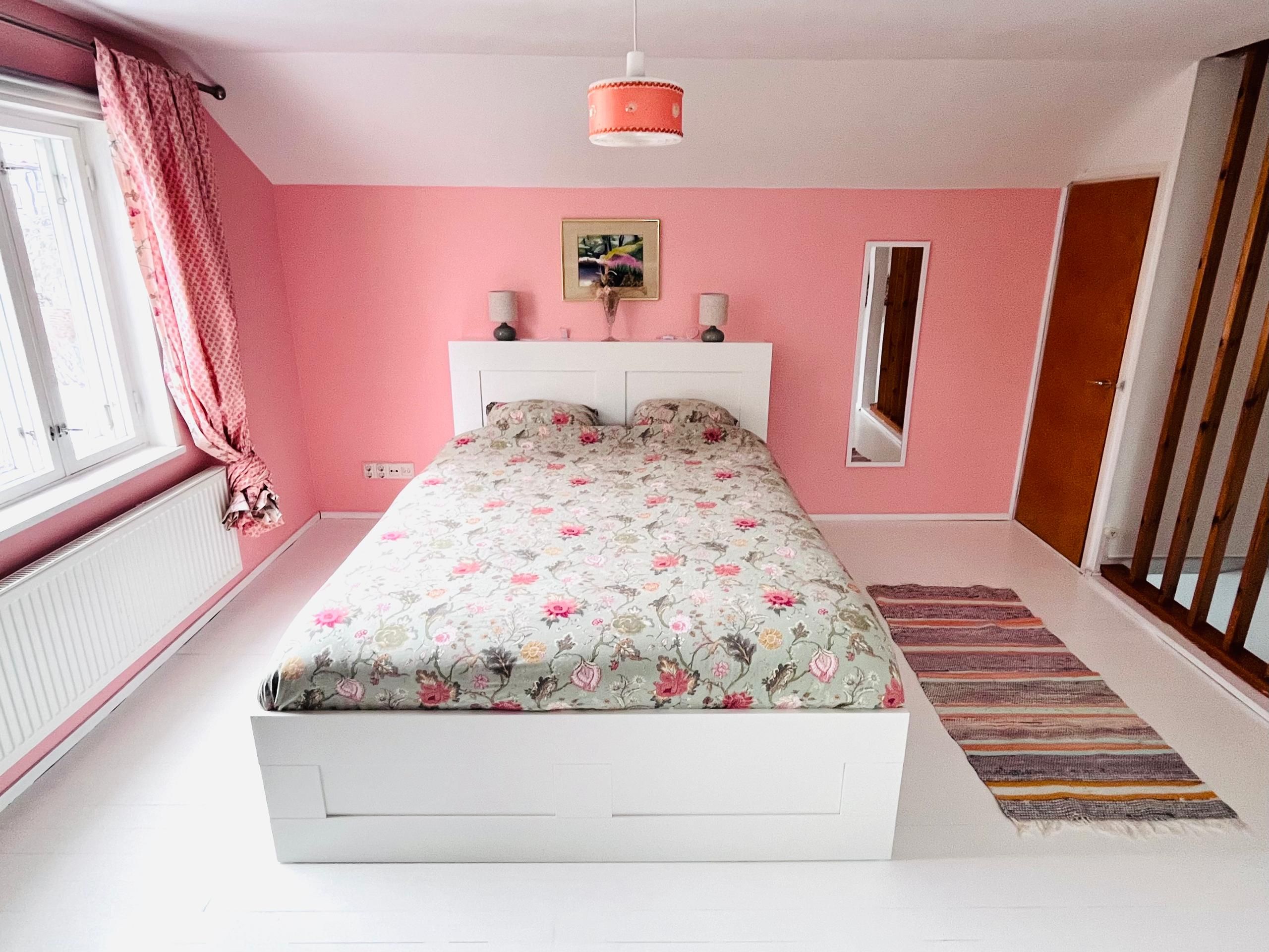 A bedroom with a bed, a window, a mirror, and a door.